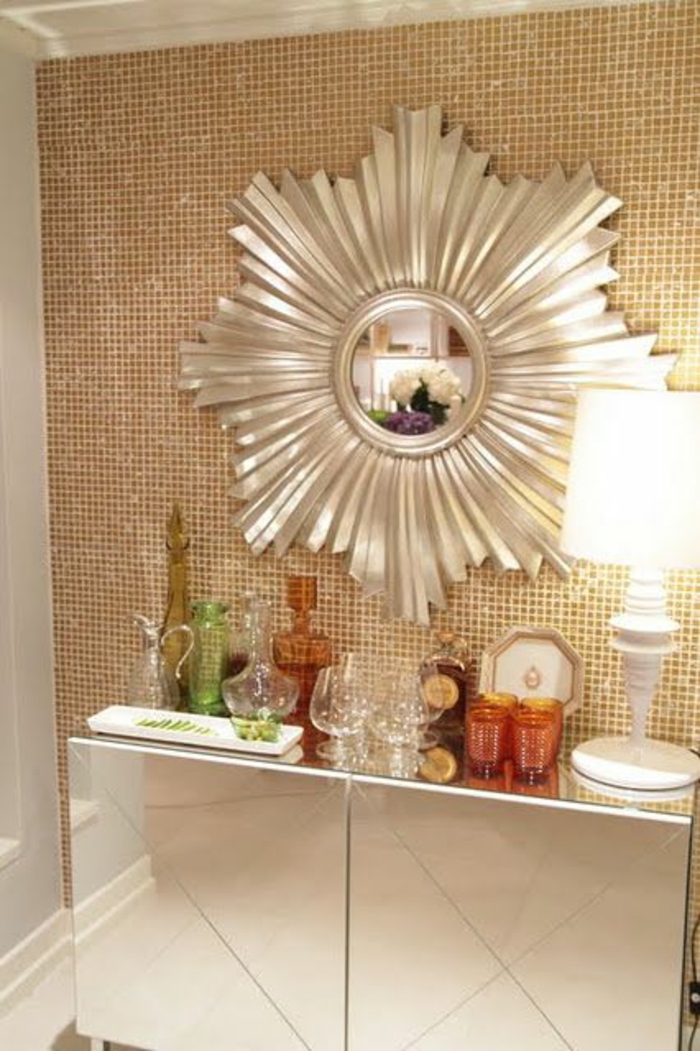 miroir de sorcière soleil aux grands rayons stylisés en couleur argent au-dessus d'un meuble en blanc laqué