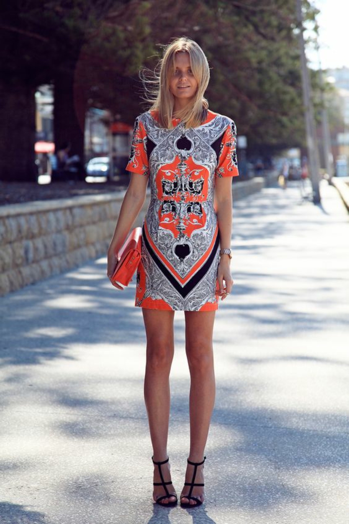 une mini-robe à l'imprimé ethnique portée avec des sandales à haut talon et sac pochette orange