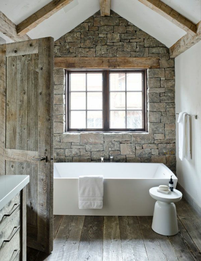 deco campagne salle de bain, mur en pierre, parquet et porte bois brut, baignoire à poser, poutres apparentes, serviette blanches