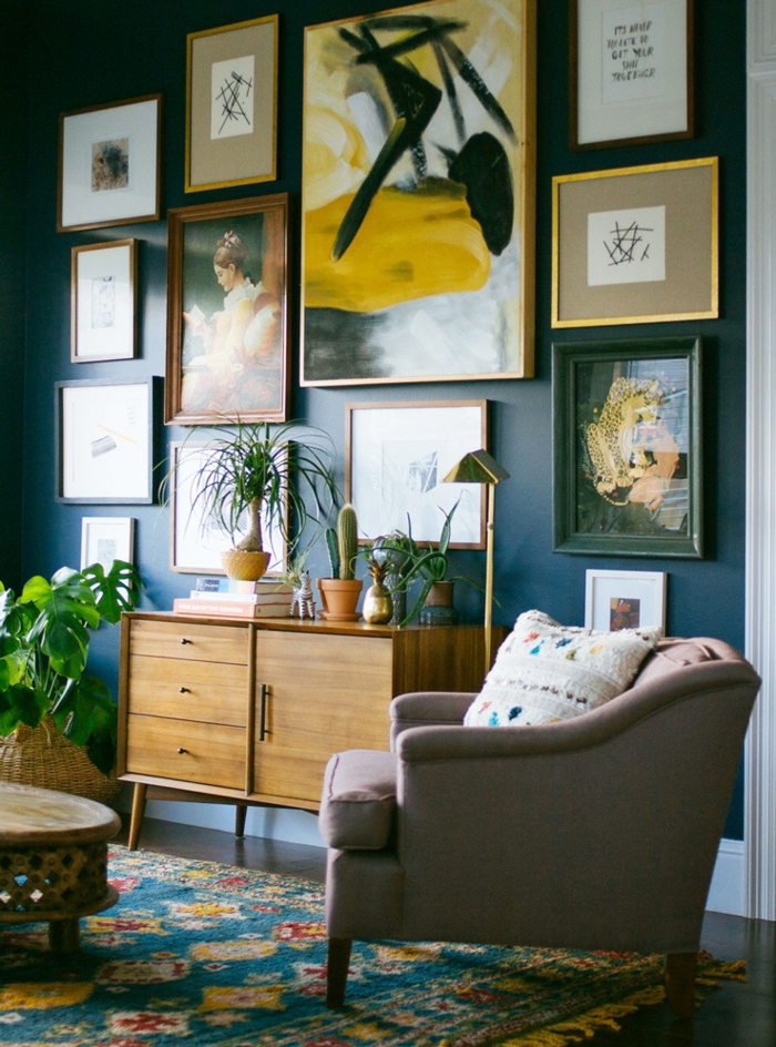 un salon bohème chic au mur bleu canard décoré de cadres, des nuances de l'ocre jaune sur le mur