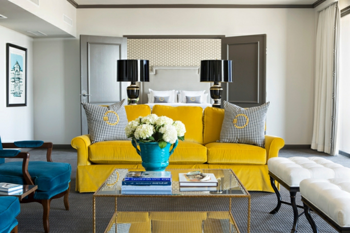 deco bleu et jaune dans un salon contemporain, chaises bleu canard, canapé jaune, table basse, tapis gris, tabourets en bois coussins blancs, lampes noirs stylées