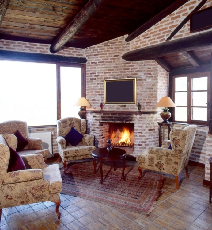 mur en briques, sol en pierre, fauteuils vintage, petit tapis oriental, table basse en bois, maison ossature bois, salon rustique