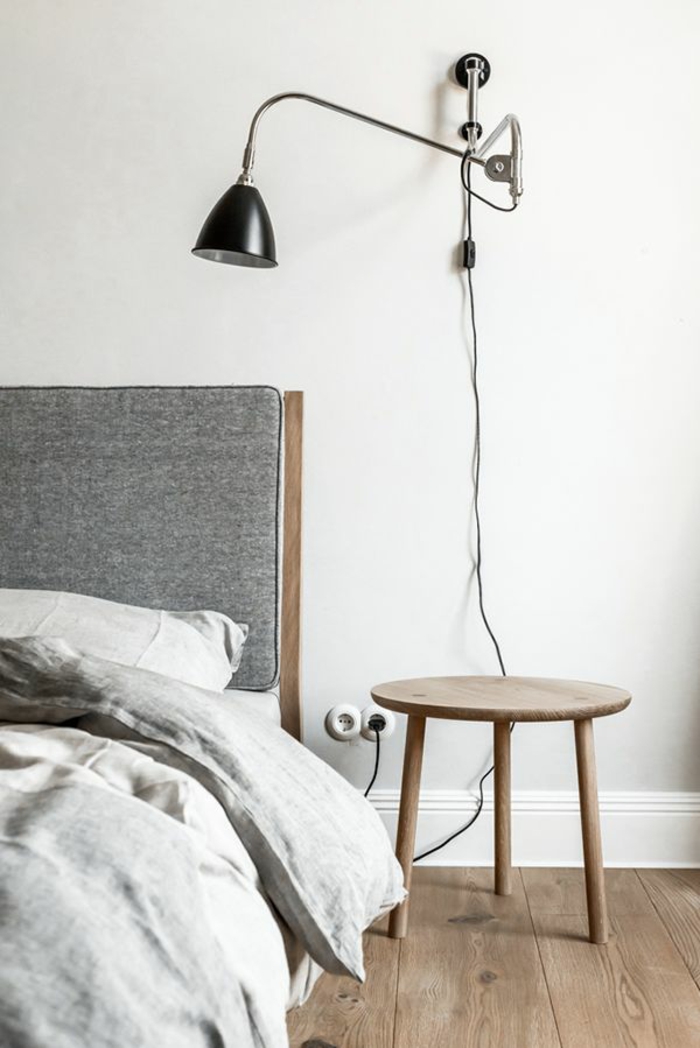 une lampe d'applique avec bras réglable au-dessus d'un trépied en bois naturel, chambre à coucher monochrome