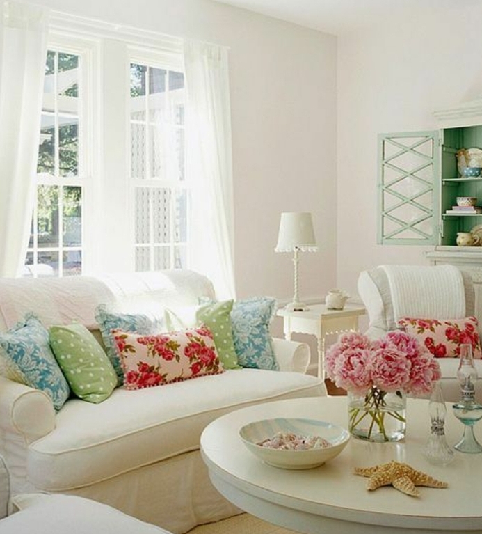 canapé et table en bois blancs, coussins multicolores, bouquet de pivoines, vaisselier vert pastel, rideaux blancs