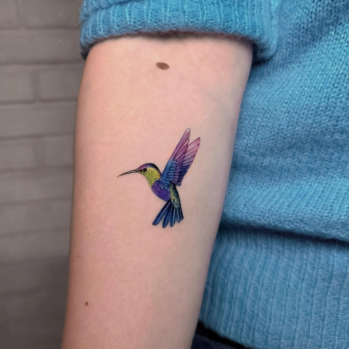 tatouage colibri colore sur bras femme pull bleu dessin sur peau