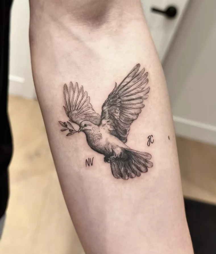 tatouage colombe realiste sur bras homme ailes vol branche feuilles initiales