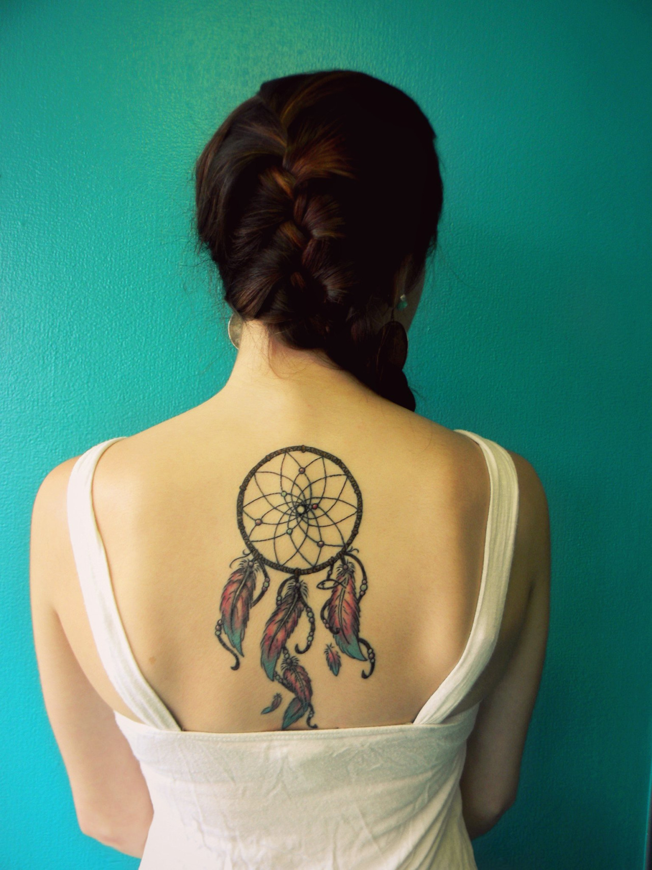idée de tatouage attrape reve sur le dos, filet et cerceau rond, plumes en bleu, rouge, jaune et orange, femme tresse sur le coté