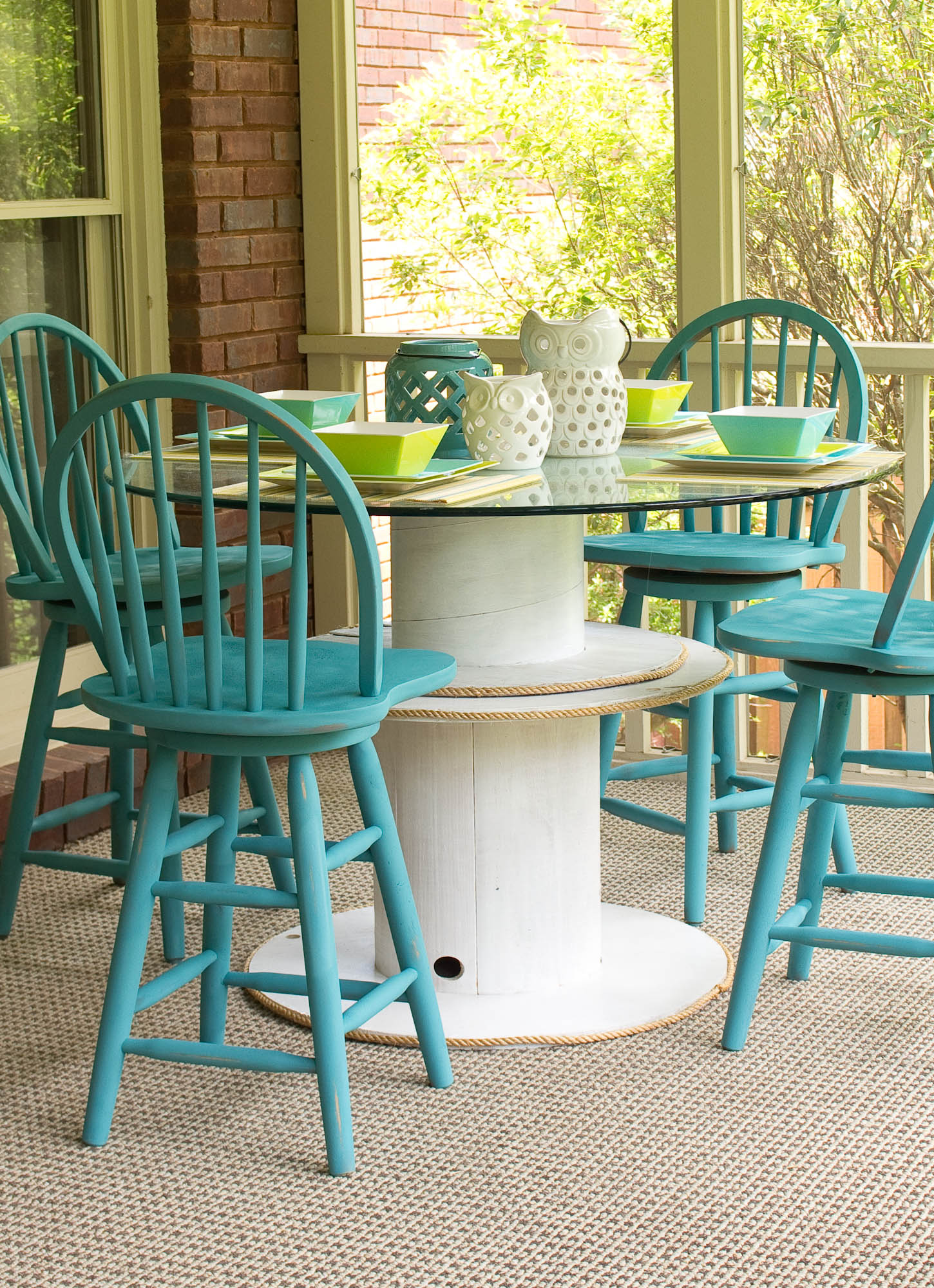 table en touret blanche avec un plateau en verre, chaises en bois bleus, tapis gris, amenagement terrasse