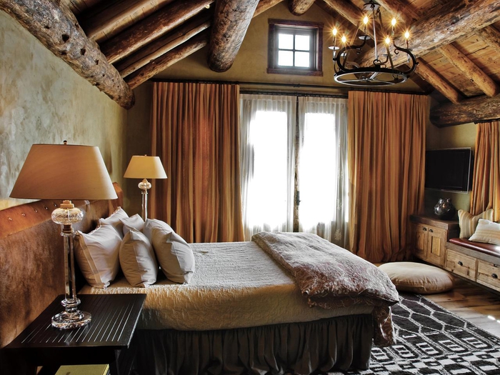 une chambre à coucher rustique aux tons neutres, ambiance de style chalet aux tons neutres, rideaux couleur terre sienne, chambre sous pente aux poutres apparentes en bois rustique