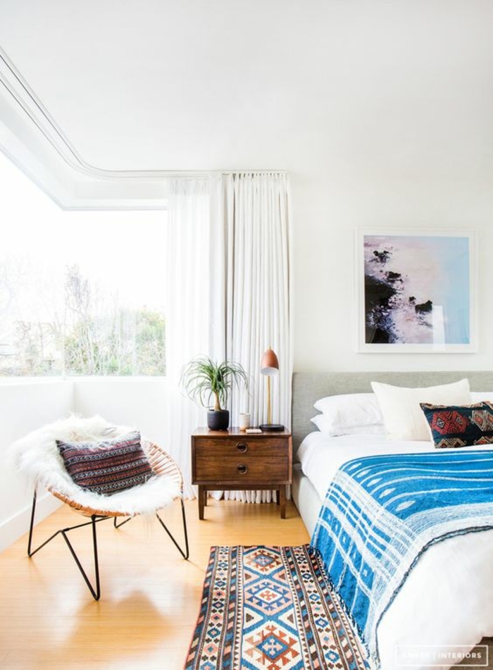 chambre à coucher blanche, tapis ethnique, plaid de lit bleu, peinture abstraite, chaise papasan
