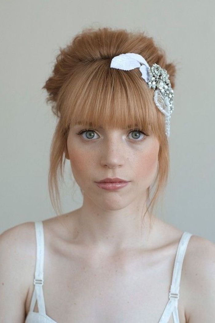 une coiffure de mariée relevée avec frange et joli accessoire avec strass, cheveux blond roux associé à un teint de pêche