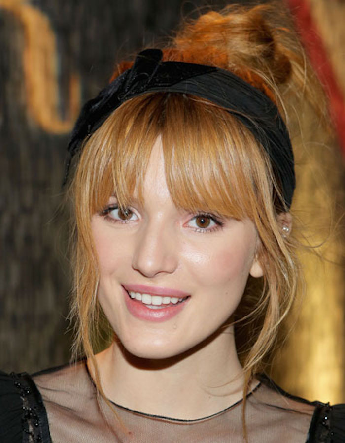 une coiffure relevée girly avec frange et chignon haut flou accessoirisé d'un head band, des cheveux roux vénitien