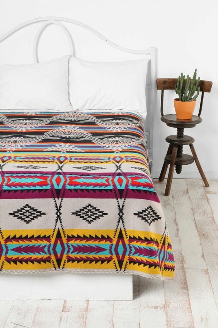 tissu ethnique sur le lit, chambre à coucher blanche, petite chaise rustique en bois