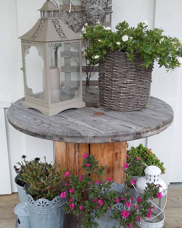 deco exterieur, table en touret, decoration lanterne grise, bougie, plante et fleurs, panier en bois, amenagement terrasse