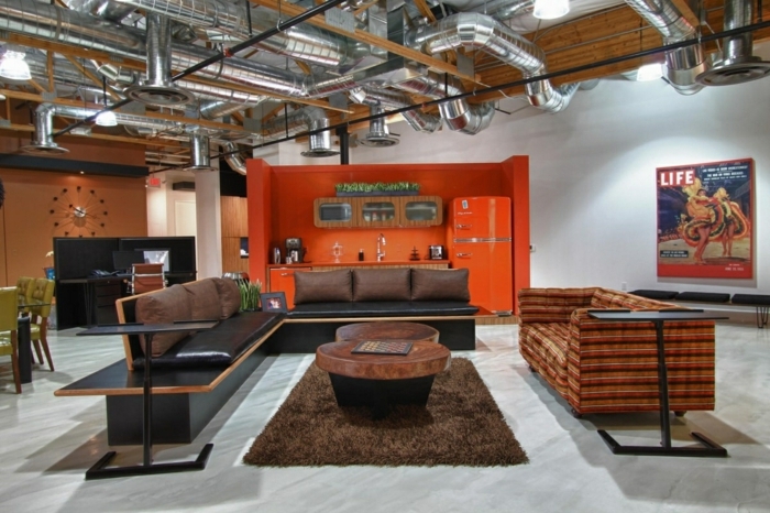 meuble noir et bois, pipes apparents, cuisine orange, horloge, fauteuil vert, canapé noir, table en bois, tapis moelleux