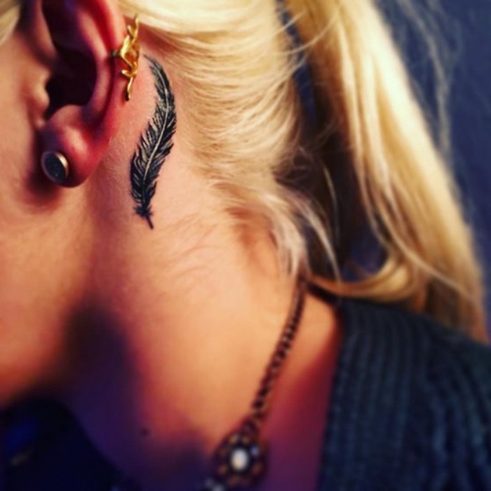 idée de petit tatouage femme, derrière oreille, une plume noire, femme blonde, tattoo élégant