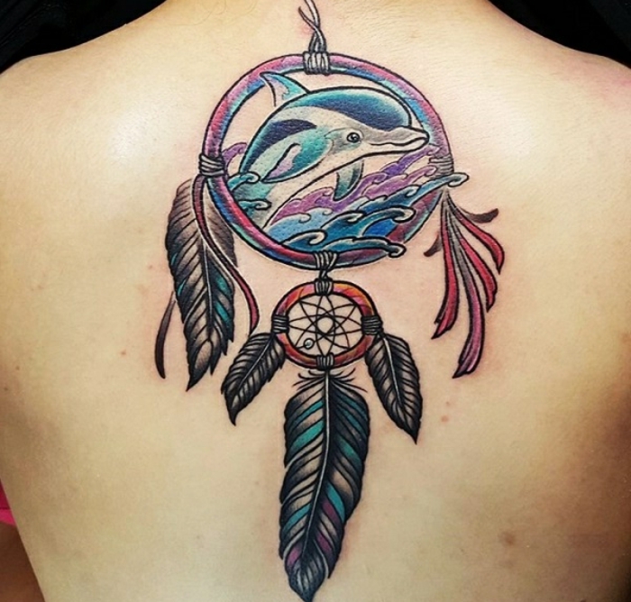 tatouage attrape reve sur le dos, grand cerceau avec in dauphin à l'intérieur, flots de mer, plumes en mauve bleu et noir