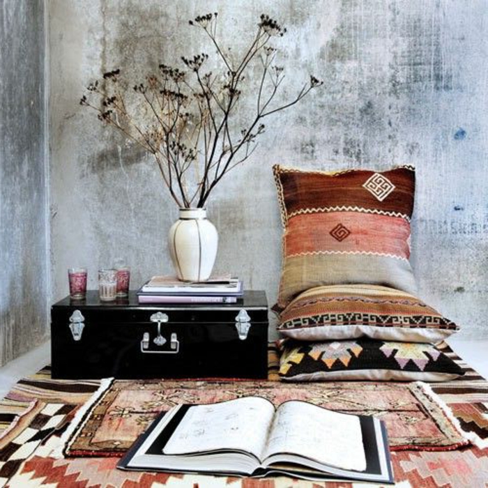 tissu ethnique, coussins aux motifs géométriques, enduit gris, vase avec fleurs sèches
