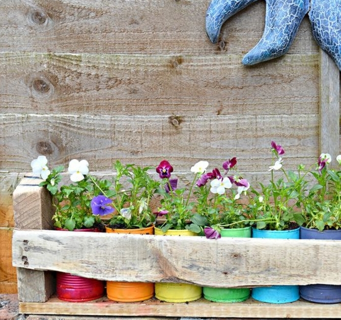 idée de jardiniere palette, en planches de bois brut, des boites de conserve repeintes, colorées et diverses fleurs plantées dedans