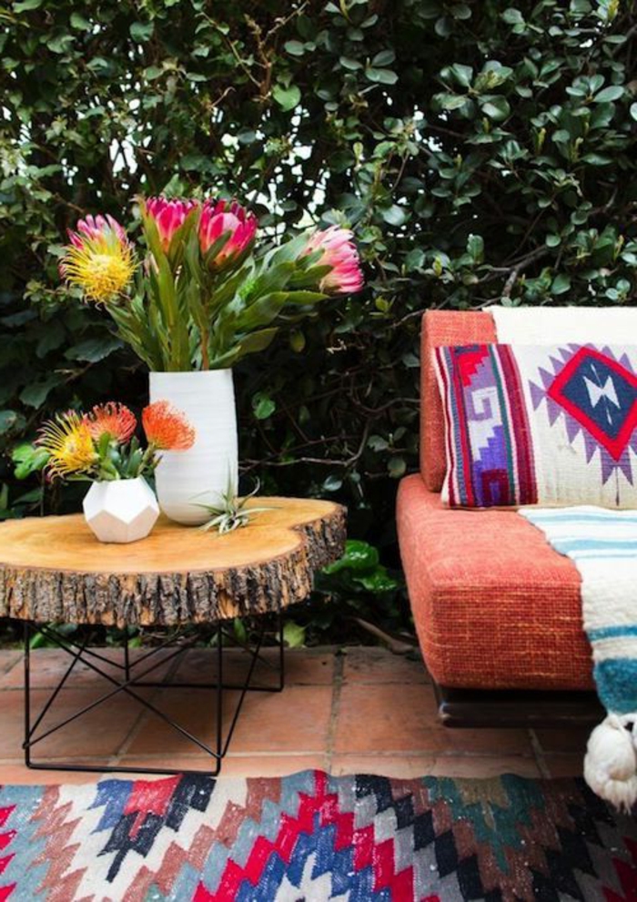 motifs aztèques, sofa orange, table tronc d'arbre, vases avec des fleurs, tapis en rouge et bleu