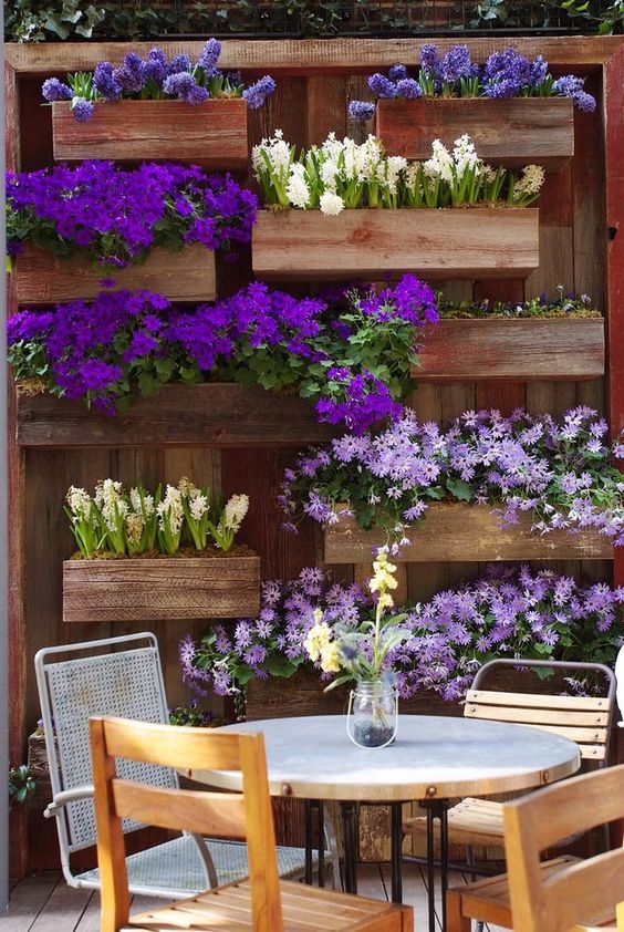 jardiniere palette, plusieurs bacs a fleurs, avec des fleurs printanières rangées contre un mur en bois exterieur