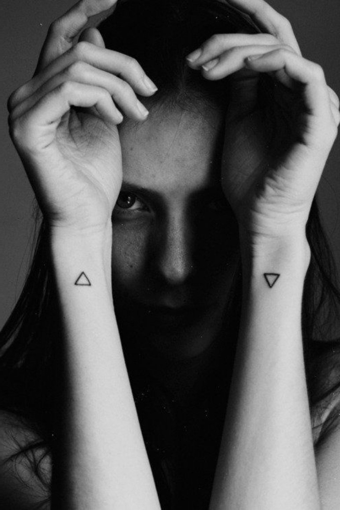 petit tatouage femme sur le deux poignets, style graphique, encre noire, fille enigmatique, triangles noirs