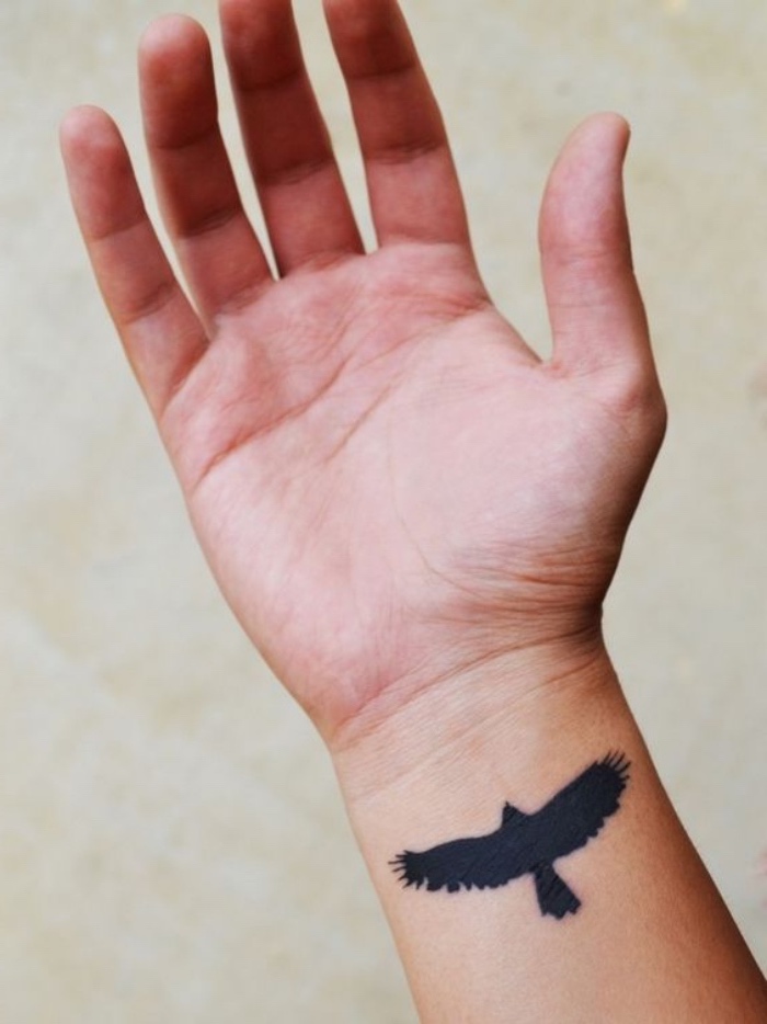 modèle de petit tatouage homme tribal, aigle silhouette noire sur le poignet, style tribal