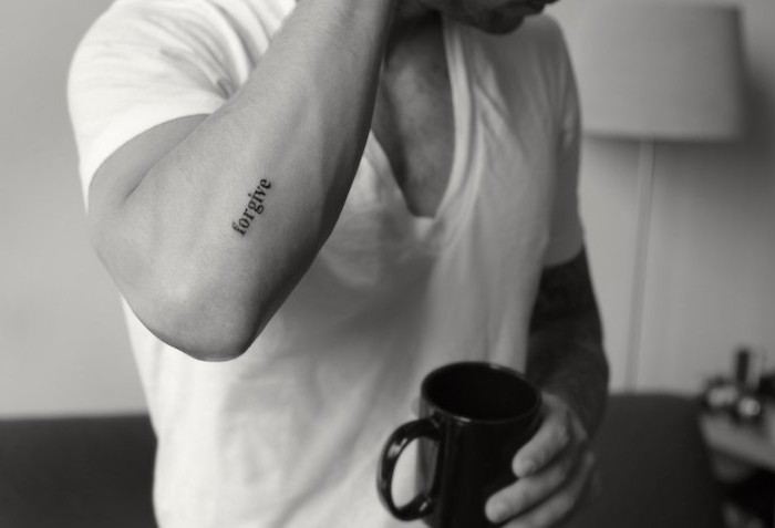 tatouage homme, lampe blanche sur pieds, canapé, tasse de café noire, tatouage mot sur l'avant bras
