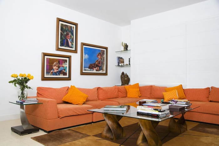 un intérieur blanc rendy plus dynamique grâce au canapé couleur sienne orangé et le mur en cadres