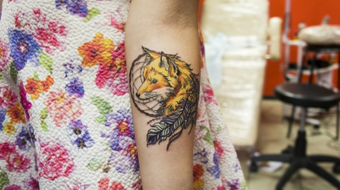 tatouage attrape reve avant bras, capteur de reve noir, plumes en jaune et mauve, et dessin de renard jaune orange
