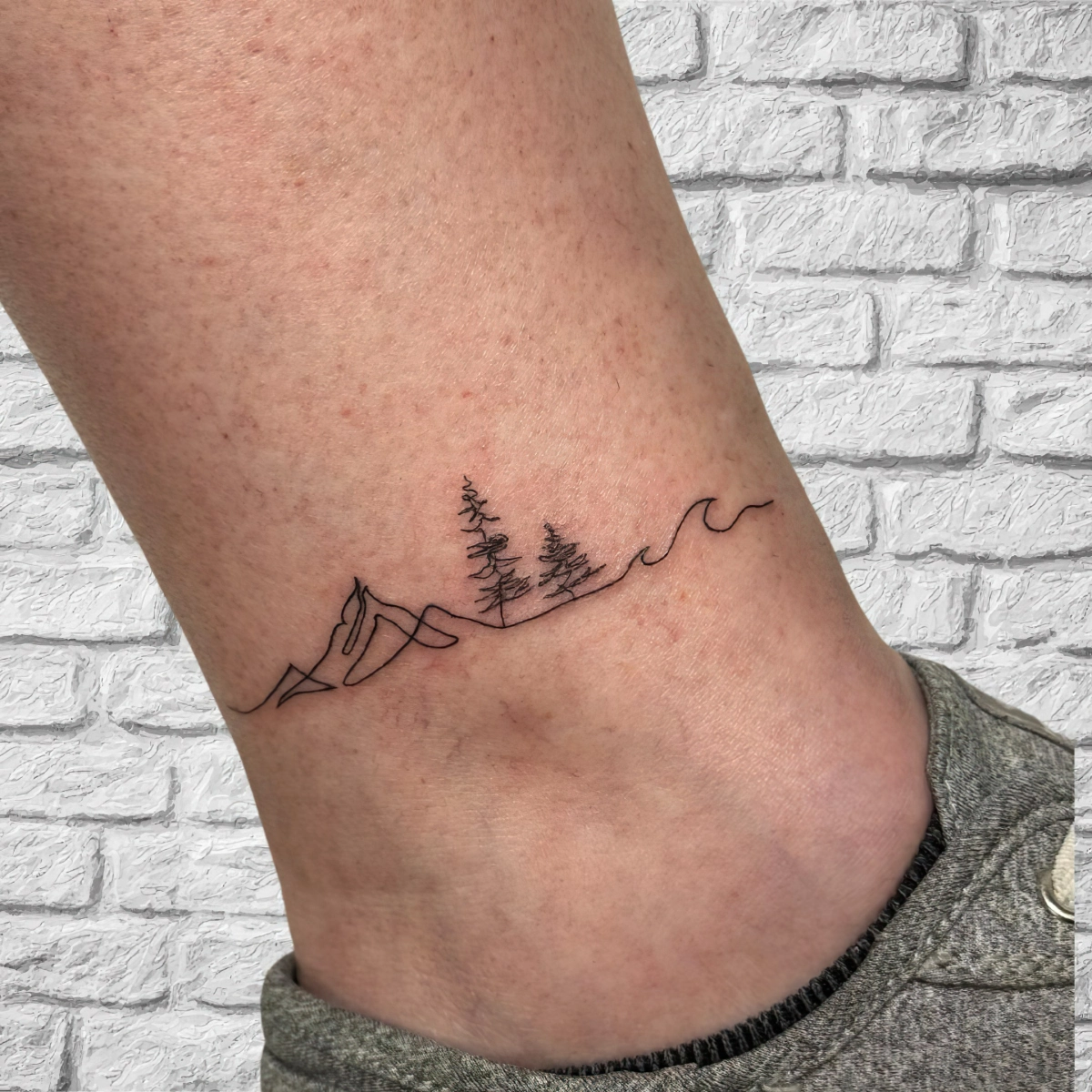 tatouage cheville minimaliste ligne courbes vague foret arbres
