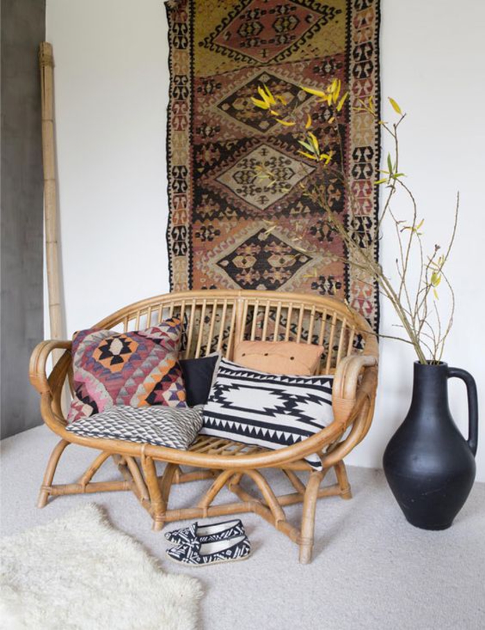 une fauteuil en bambou décorée de coussins de style ethnique chic, tenture ethnique chic comme une décoration murale originale