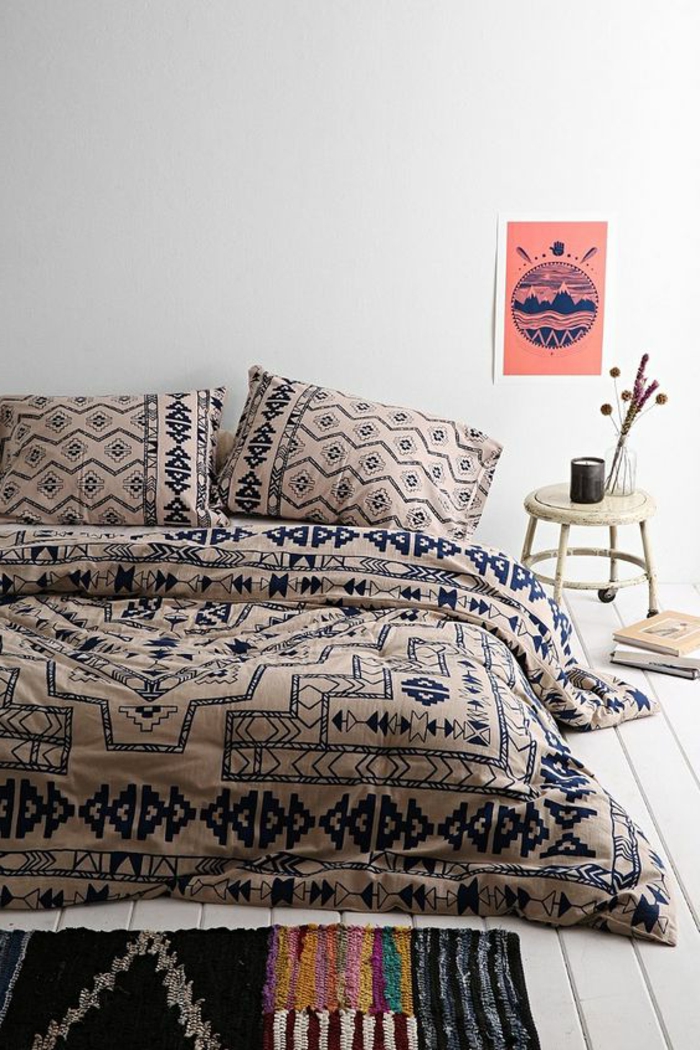tissu ethnique sur le lit, sol en planches de bois, petit chevet sur roulettes, carpette exotique