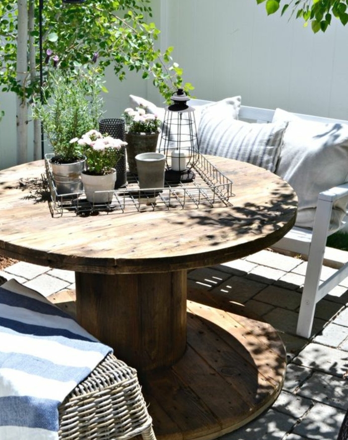 amenagement jardin, table en touret bois marron, banc blanc, coussins decoraifs, centre de table floral vintage, chaise en rotin