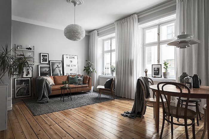 tableau scandinave, murs peints en gris, rideaux longs en blanc, tapis rectangulaire en gris, canapé en cuir marron