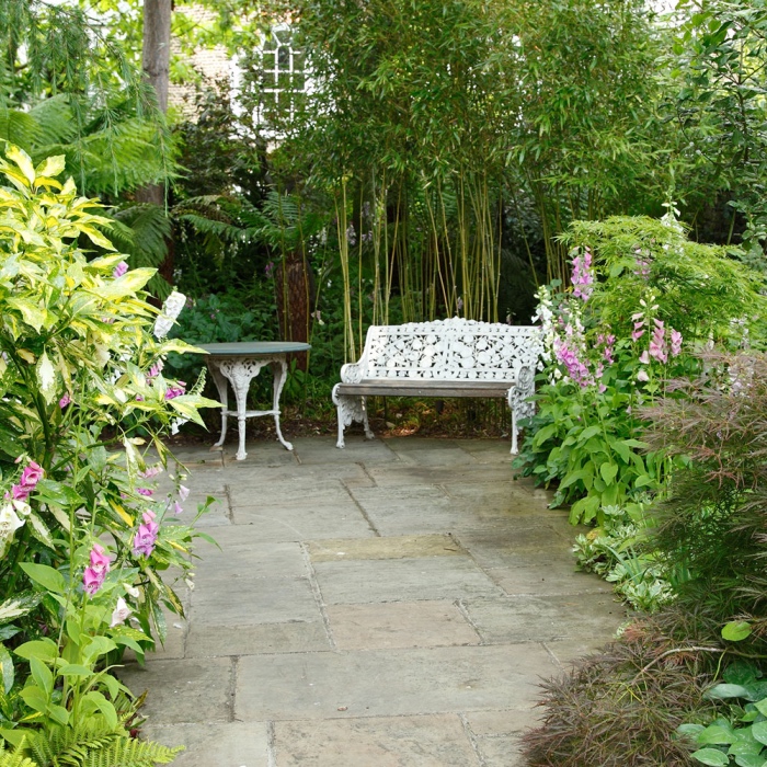 paysager son jardin, un espace revêtement en pierres, banc vintage blanc et table ronde de jardin, bambou et plusieurs arbustes fleuris