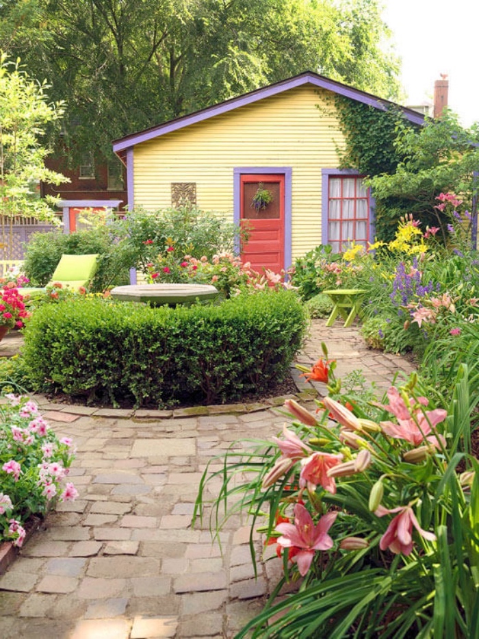 amenagement petit jardin avec des chemins de pierre, une fontaine entouré de buis, parterre de fleurs, chaise longue dans la cour d une petite maison de campagne