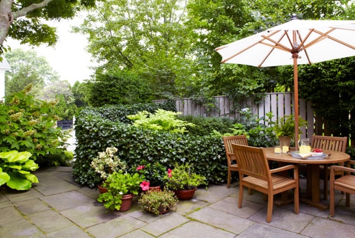 amenagement jardin avec patio de dalles de béton, chaises et table en bois, parasol, buis et pots de fleurs, palissade en bois