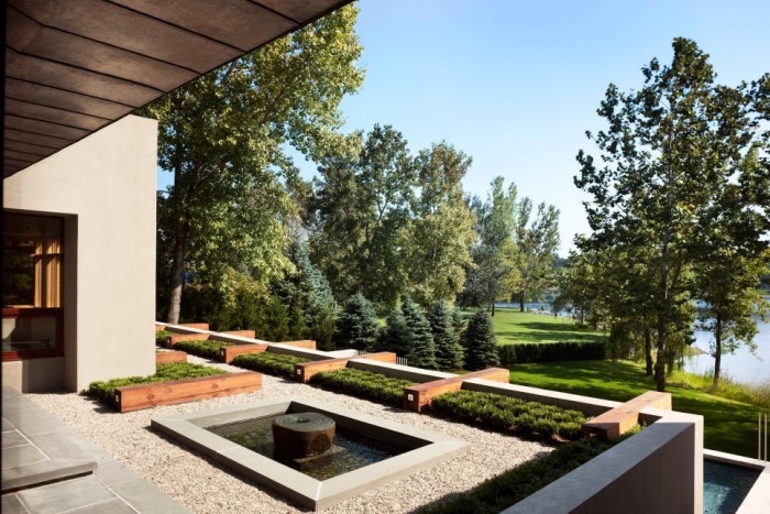 amenagement jardin paysager, terrasse revêtement de gravier avec fontaine d eau et bassin, un gazon avec des buis et arbres, petite piscine d eau