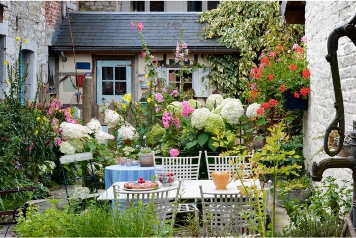 amenagement petit jardin fleuri avec beaucoup de fleur et d arbustes fleuris et plantes grimpantes, coin repas a l exterieur avec table et chaises blanches