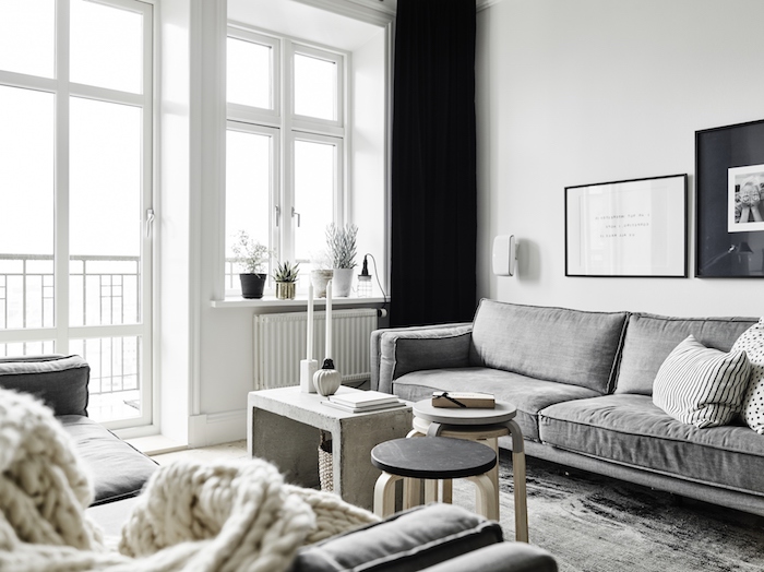 intérieur scandinave, cadres photo en noir, canapé en tissu gris, plaid beige en crochet, murs peints en blanc