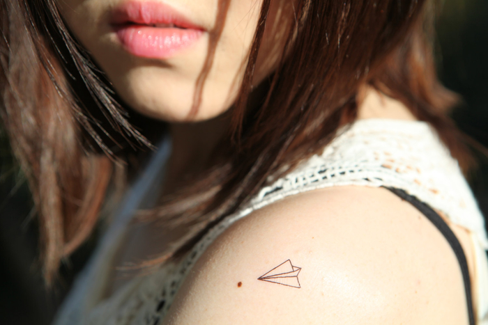 un tatouage minimaliste minuscule à l'épaule en forme d'avion en papier façon origami