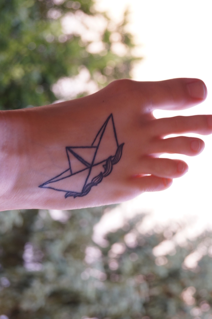 tatouage géométrique représentant un bateau en papier flottant sur les vagues