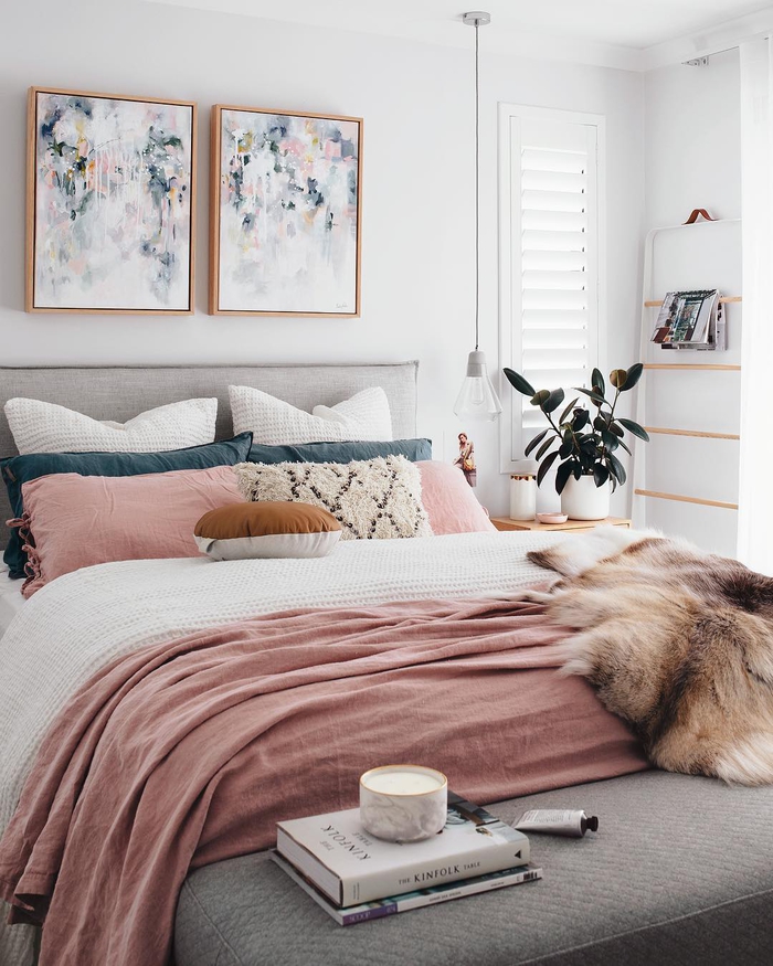 ambiance douce et féminine dans une chambre à coucher rose pastel, coussins bleu paon et rose qui reprennent les teintes des peintures