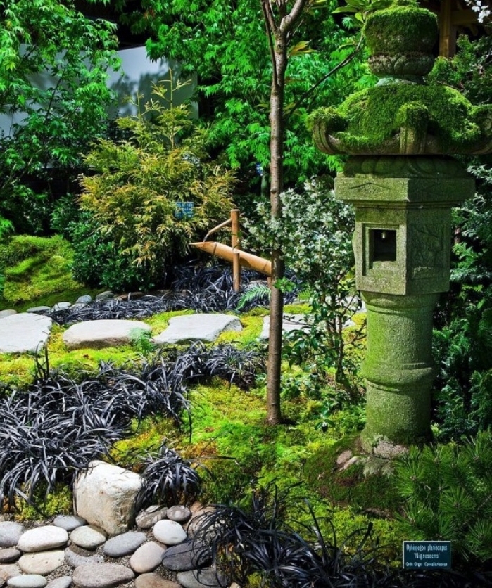 decoration zen dans le jardin, une lanterne en pierre, galets et gazon pour recouvrir le sol, arbustes arbres, vegetation verte