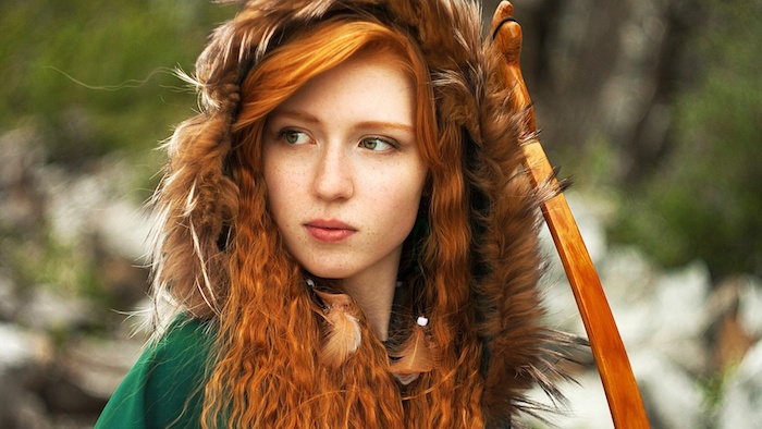 blond roux, femme dans la nature, look sauvage avec plumes dans les cheveux, manteau vert avec capeline en fourrure