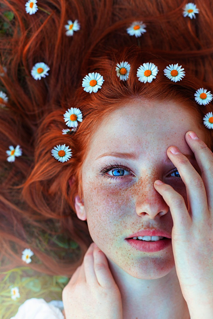 coloration roux, femme aux yeux bleus, tâches de rousseur sur le visage, coloration orange, coiffure avec marguerites 