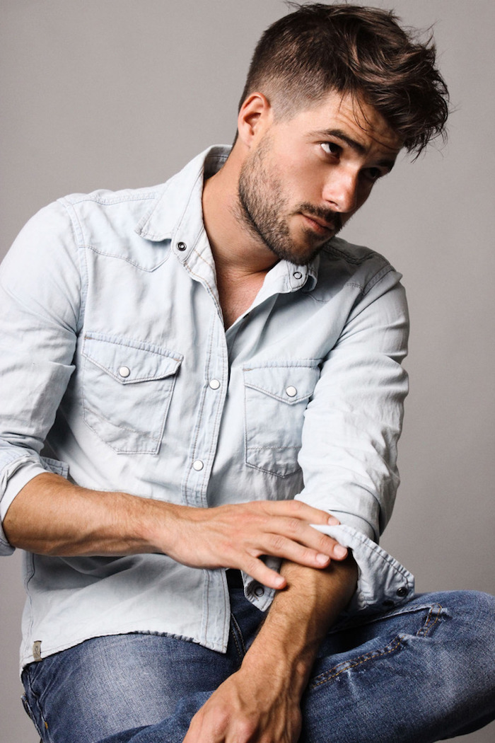 coupe-de-cheveux-homme-yeux-marron-foncé-cheveux-rasés-sur-le-cote-barbe-courte-noire-avec-moustaches coupe garcon, chemise en denim claire avec boutons blancs, paire de jeans homme, couleur de cheveux marron