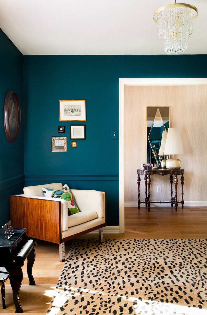 salon aux murs bleu paon foncé en contraste avec le canapé neige et le tapis imprimé à motif animalier