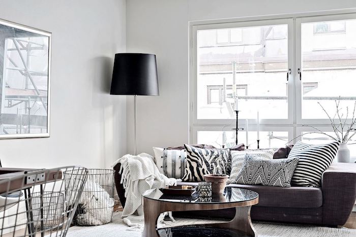 meuble scandinave, grande lampe sur pied en noir, canapé en tissu marron, coussins en blanc et noir, table en verre et bois
